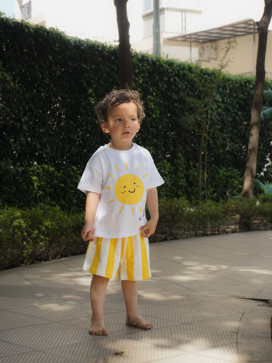 Toddler boy outdoors in Gozi's Sunny Side Up cotton T-shirt and yellow striped shorts co-ord set